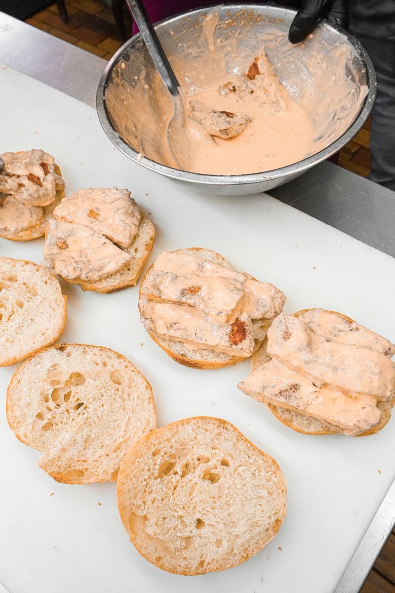Buffalo chicken salad mixed in a steel bowl beside split sandwich rolls