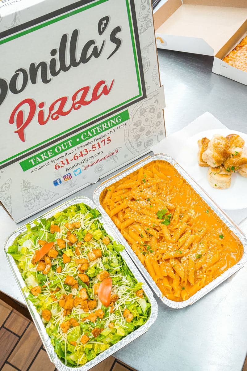 Catering trays of salad and penne alla vodka beside a Bonilla's box