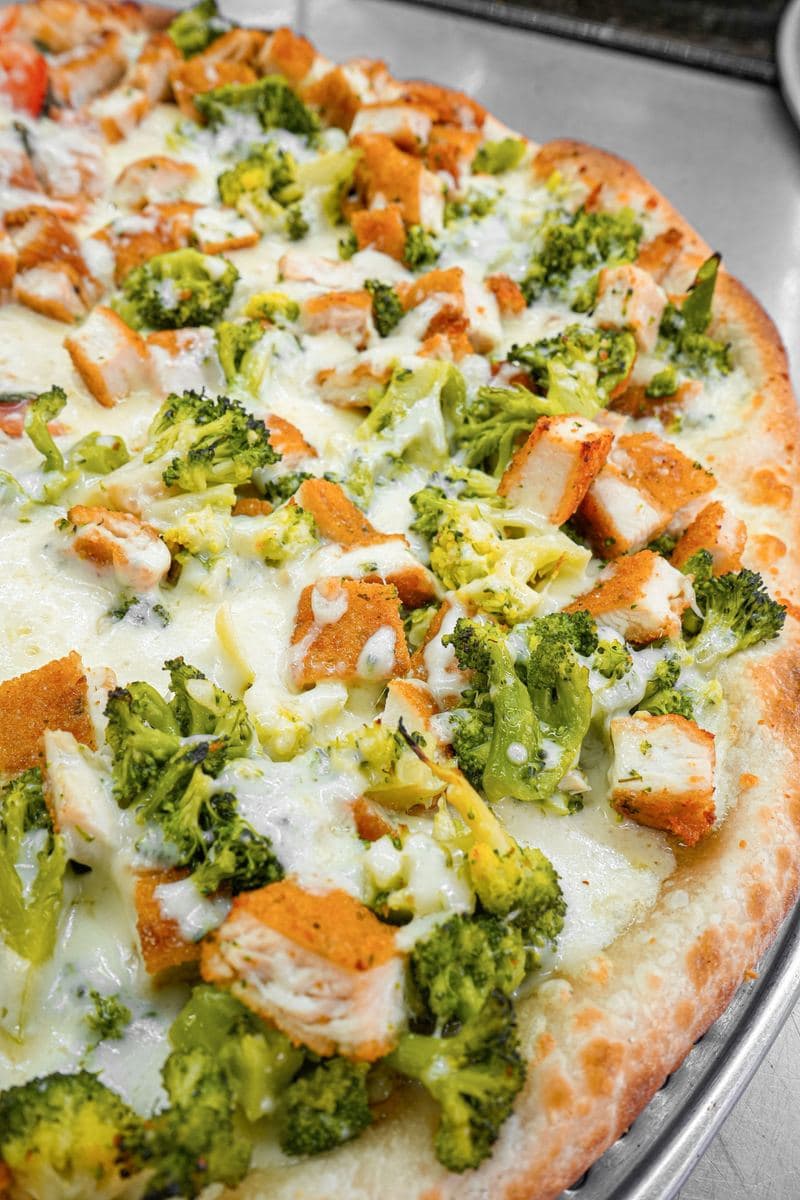 Close-up of chicken and broccoli over mozzarella on a white pie