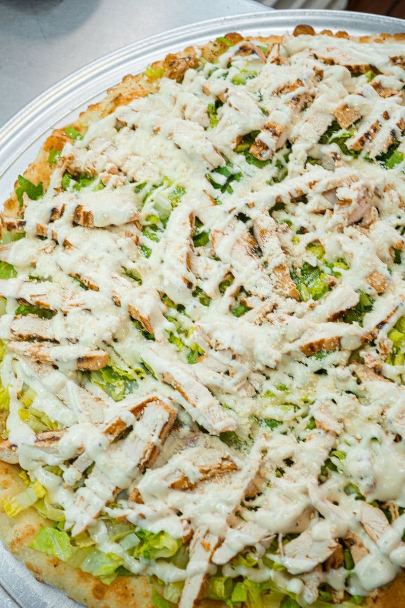 Grilled chicken Caesar salad pizza finished with Caesar dressing