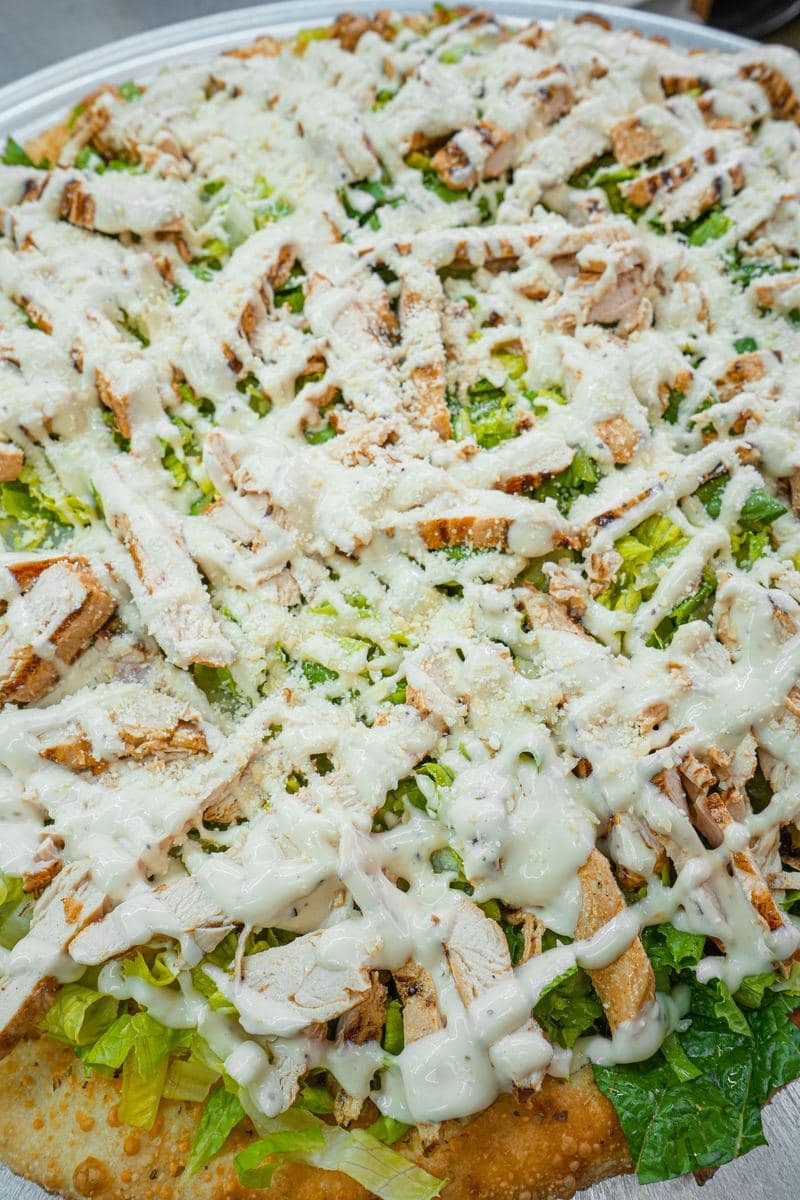 Close-up of grilled chicken and romaine over a baked crust with Caesar dressing