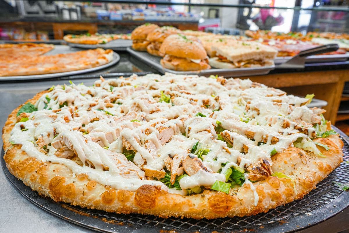 Grilled chicken Caesar salad pizza on the pan with heroes behind