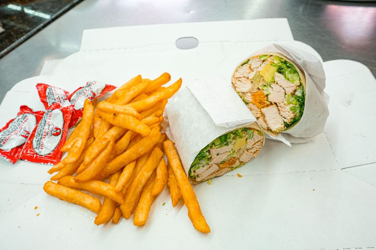 Grilled chicken Caesar wrap cut in half and served with fries