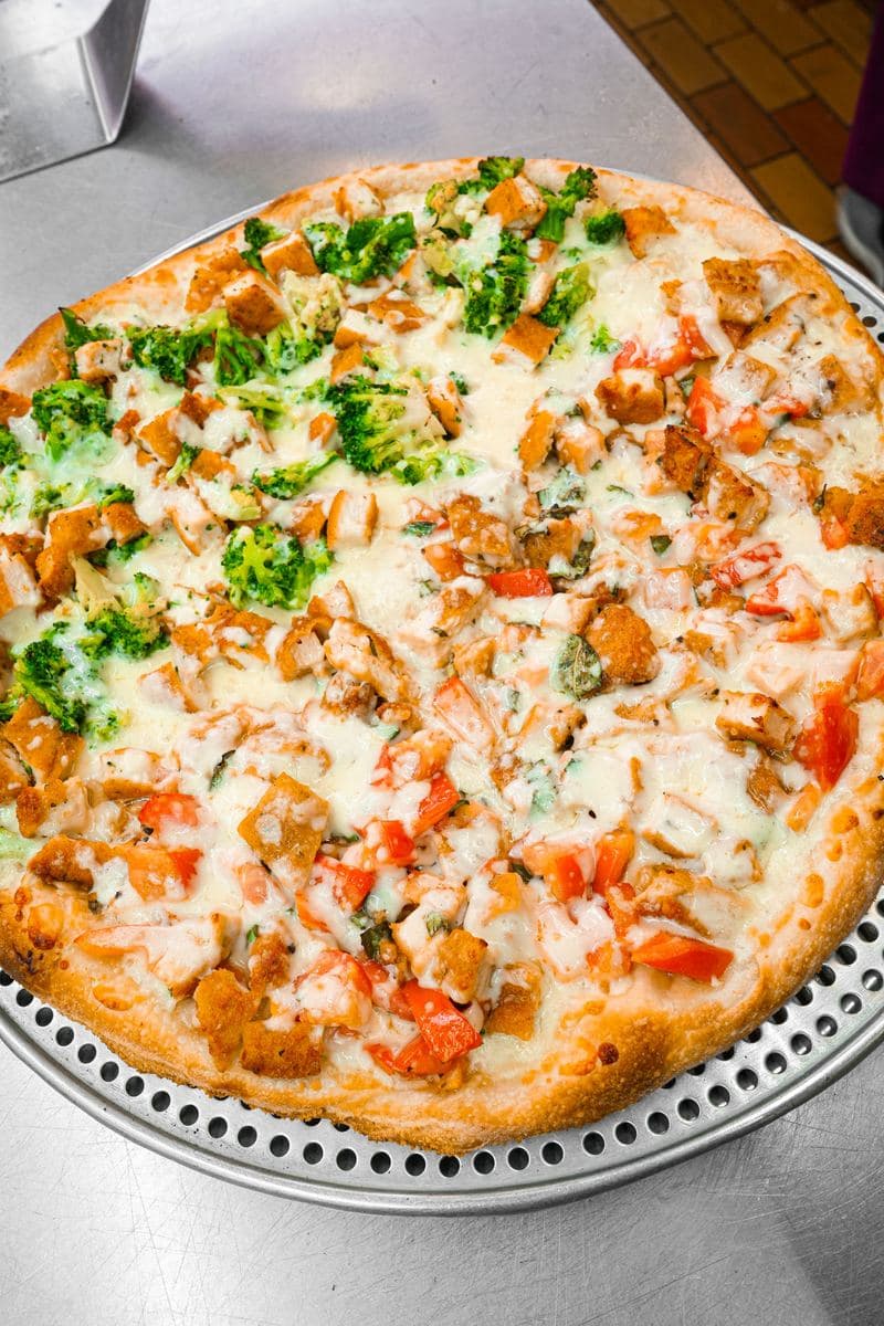 Round pie topped with chicken, tomato and broccoli