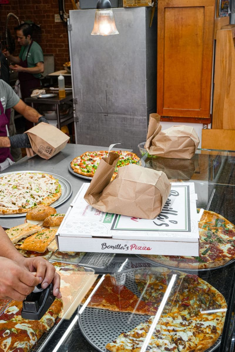 Staff bagging a takeout order at the counter beside stacked pizza boxes