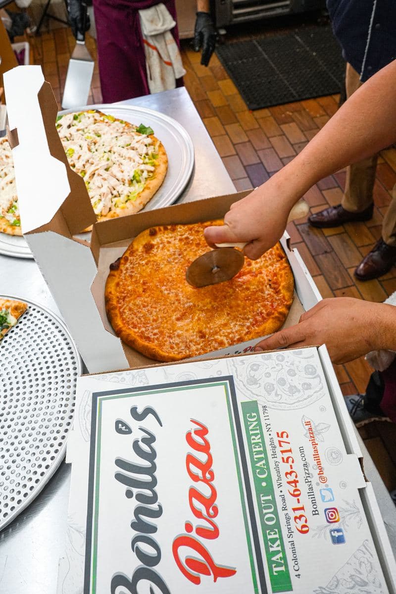 A personal cheese pie being cut in the box with a pizza wheel