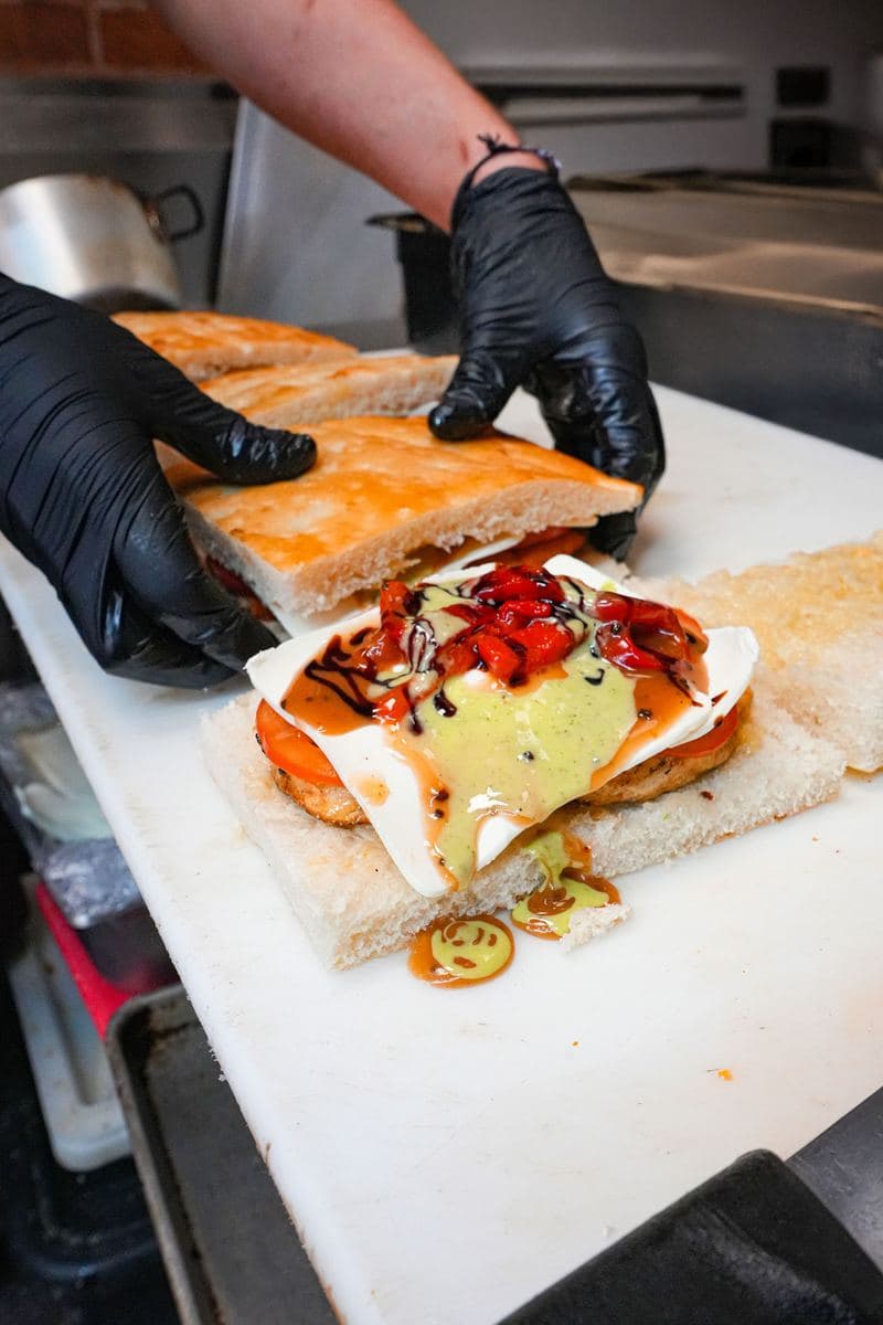 A focaccia hero being assembled with fresh mozzarella, tomato and roasted peppers