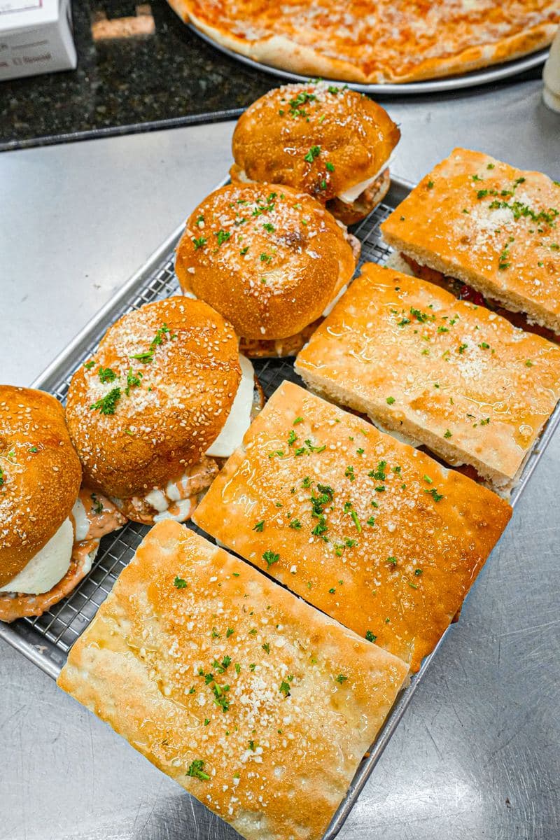 Focaccia heroes and rolls cooling on a rack, dusted with parsley