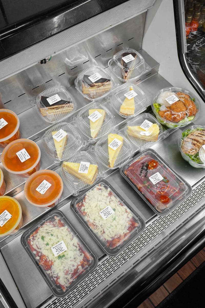 Refrigerated grab-and-go case at Bonilla's Pizza stocked with cheesecake slices, salads and prepared trays