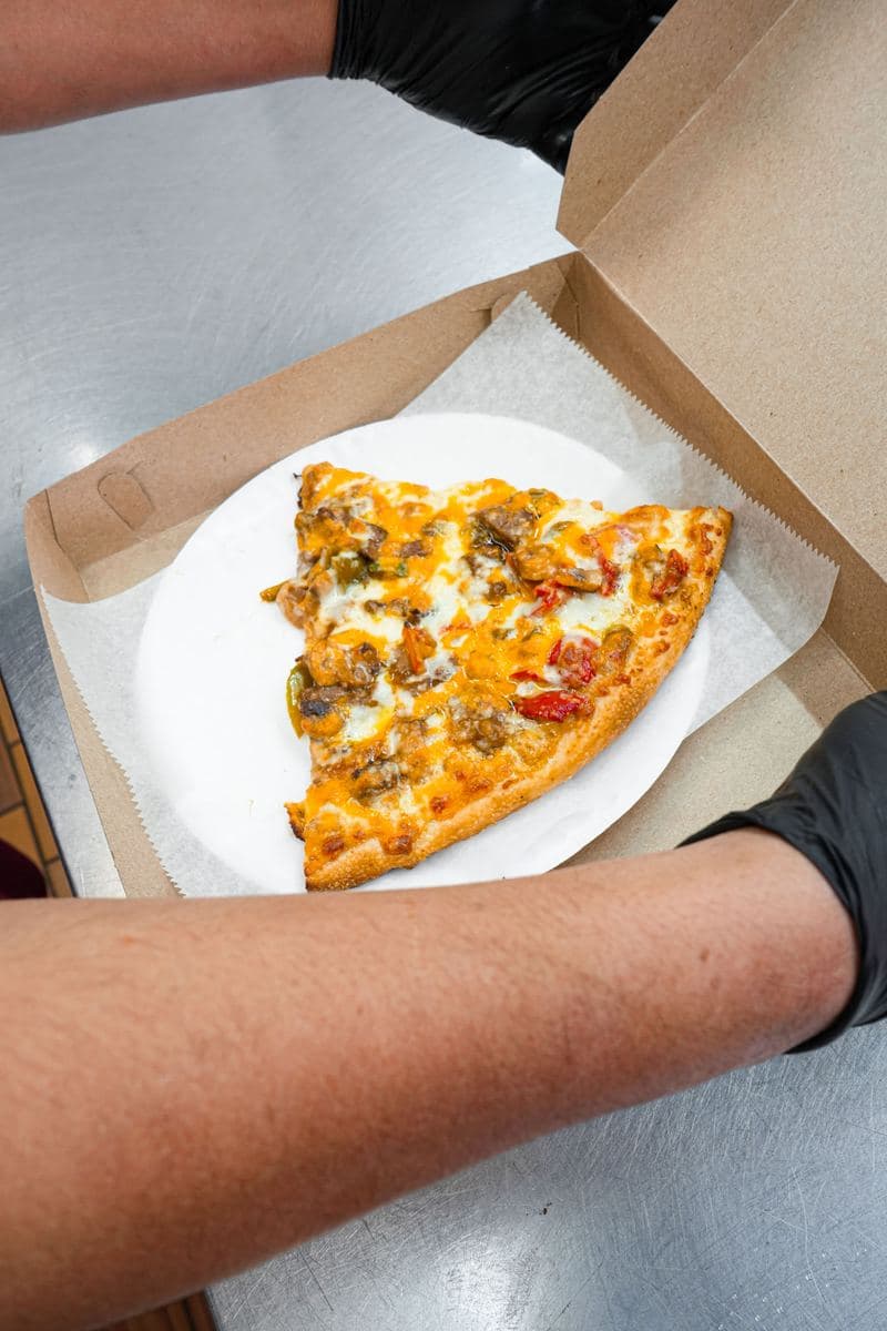 A single loaded slice served on a paper plate inside an open pizza box