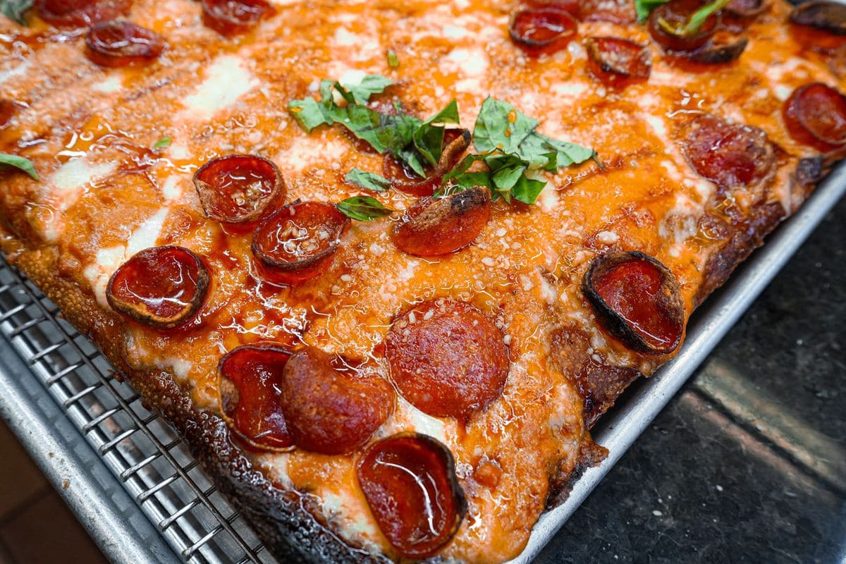 Corner of a pepperoni Sicilian with basil and a crisp caramelized edge