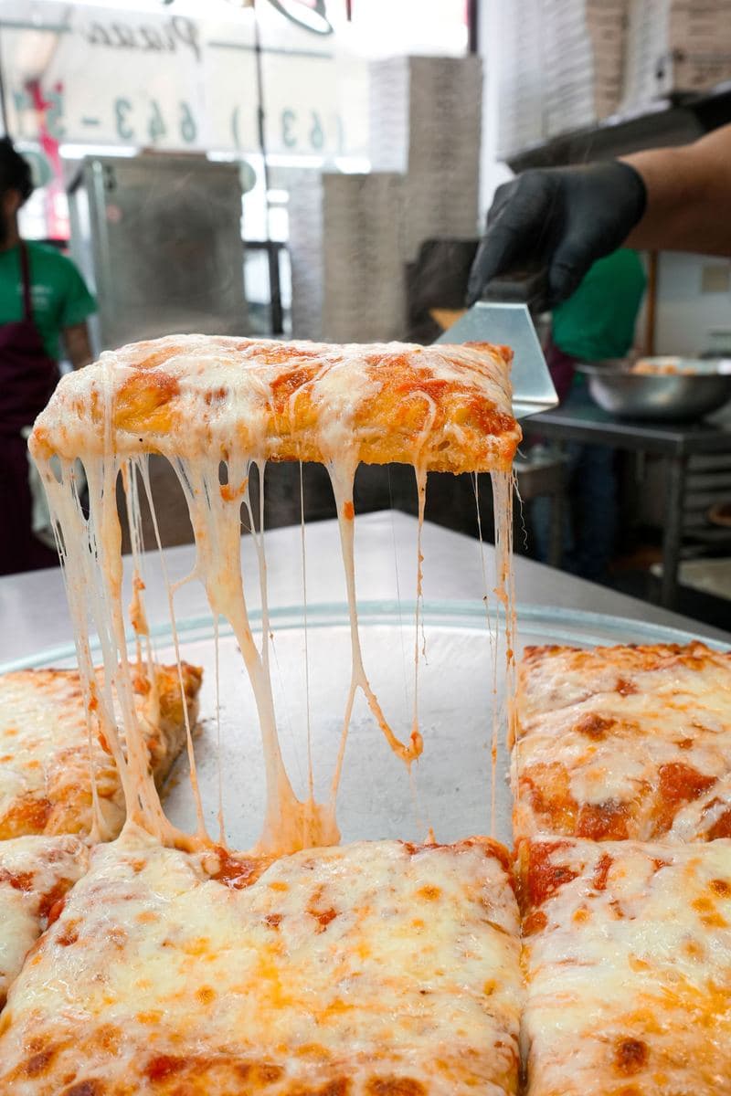A square Sicilian slice lifted from the pie, mozzarella stretching in long strands