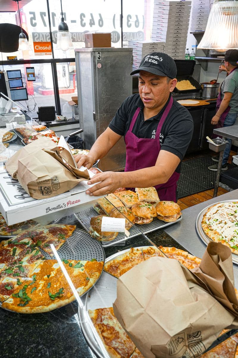 A Bonilla's staff member packing a takeout bag over a stack of pizza boxes
