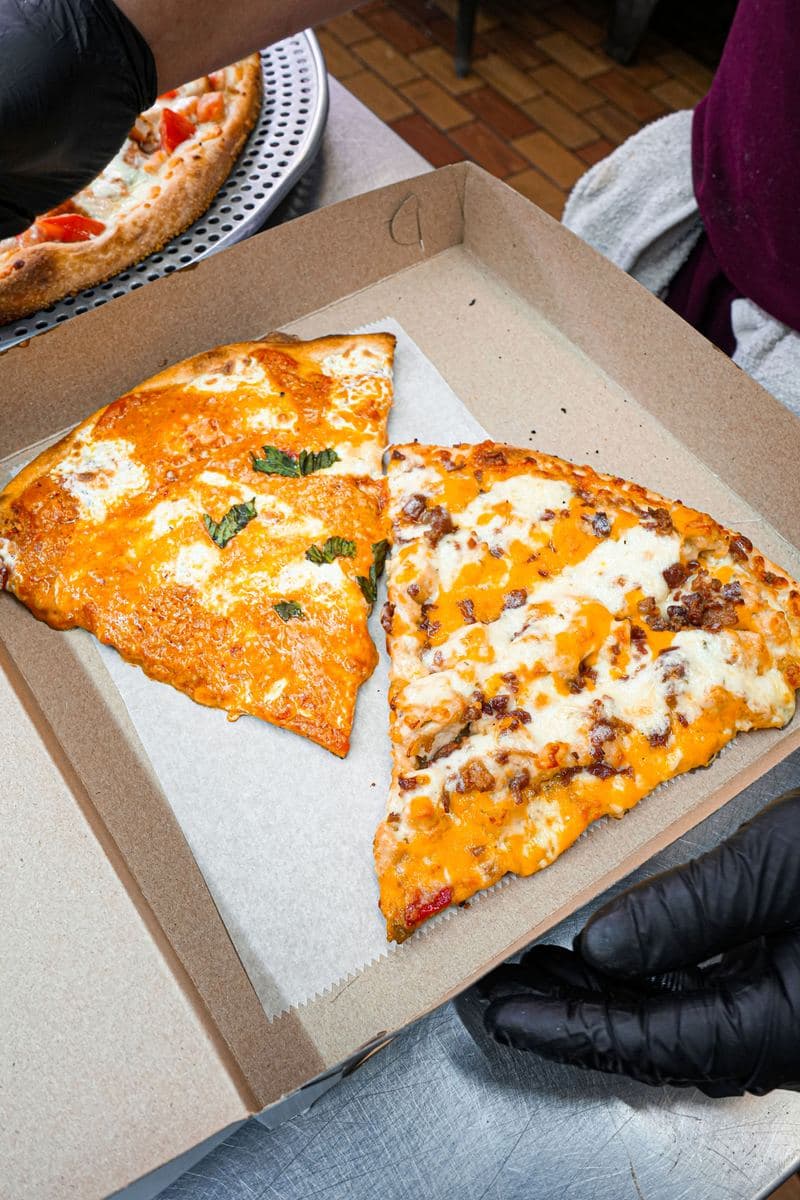 Two slices in a takeout box, one white with basil and one with barbecue chicken