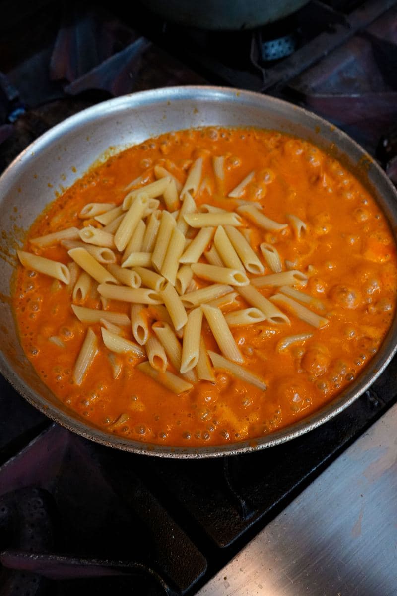 Penne dropped into a pan of simmering vodka sauce